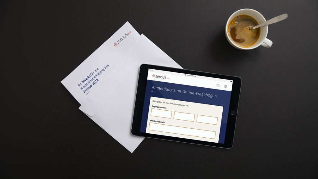 Dieses Bild zeigt die Anmeldung zum Online-Fragebogen des Zensus 2022 auf einem Tablet sowie einen Kaffeebecher